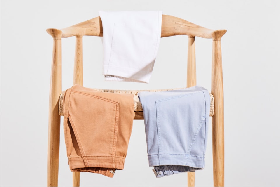 3 different colored pants hanging over a chair.